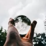 A vertical selective closeup shot of a person holding a glass ball with the reflection of beautiful green trees and the breathtaking clouds